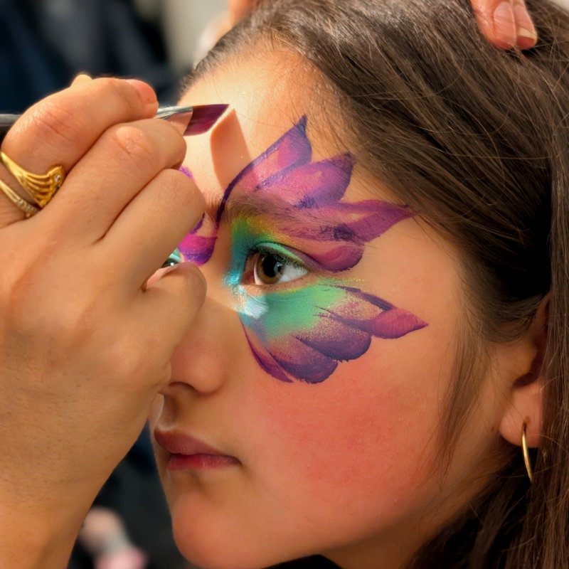 Shilpi applying intricate face paint butterfly design on a young girl