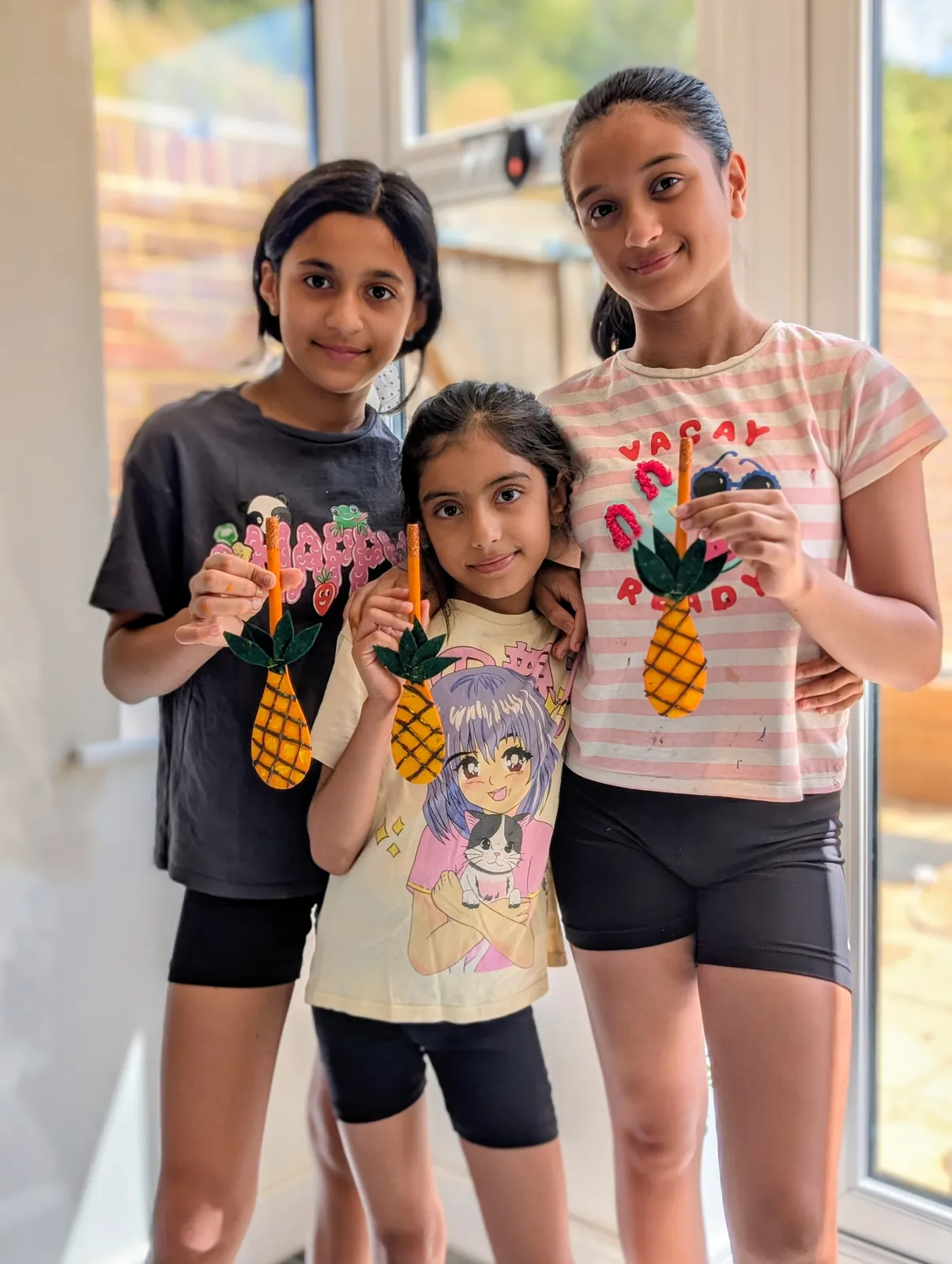Three young artists holding up the pineapple artwork they made